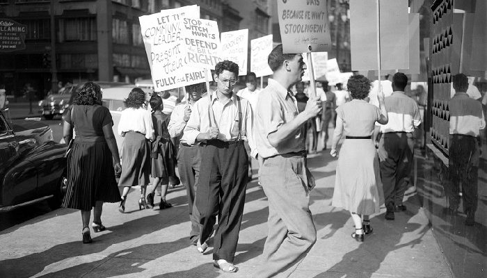 Group of people some wearing labor union emblems, carry picket signs denouncing the deportation of Sam Sweet outside the Detroit Federal Building, 1950-04-08.