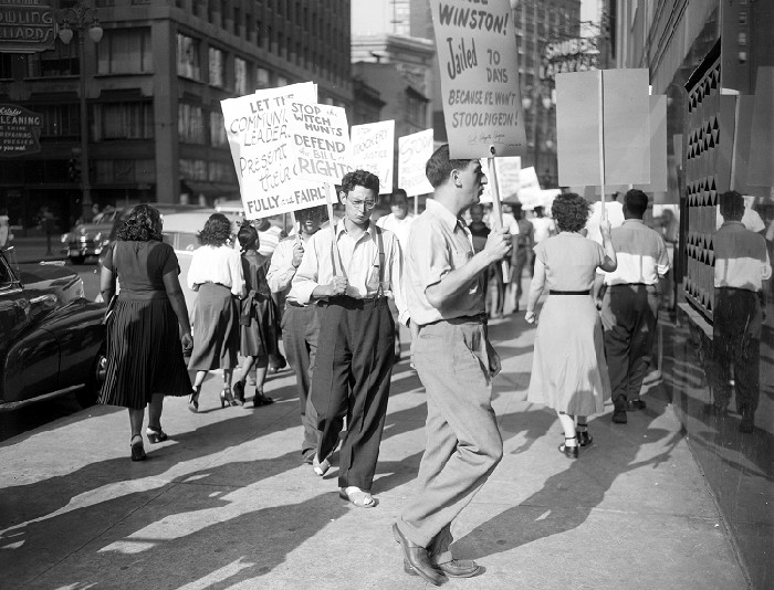 Group of people some wearing labor union emblems, carry picket signs denouncing the deportation of Sam Sweet outside the Detroit Federal Building, 1950-04-08.
